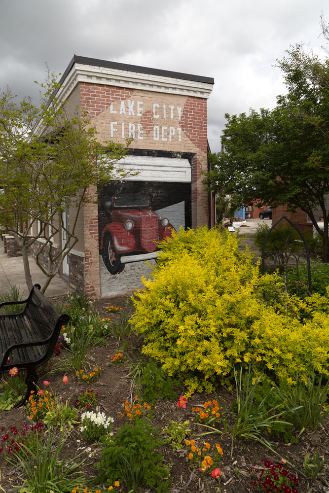 Mural depicting the Lake City Fire Department by shrubs and flowers.