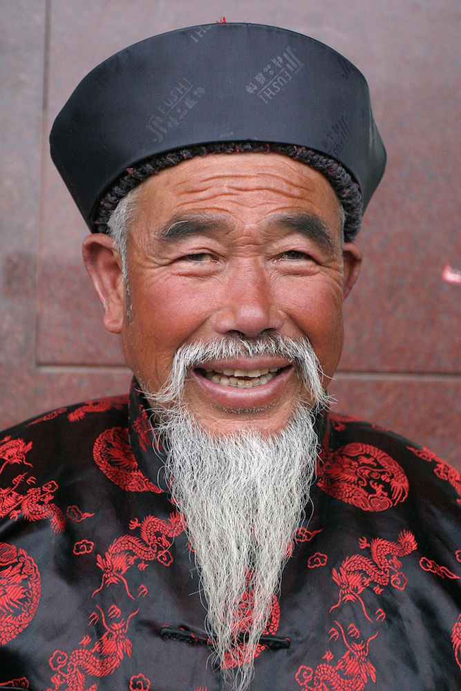 Man with a beard wearing a traditional costume in Shanghai, China, by Peter Ellegard.